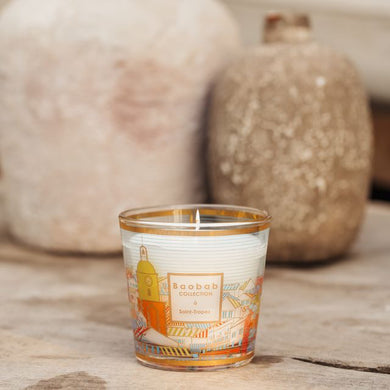 Candle in a decorative glass container on a wooden surface with ceramic jars in the background