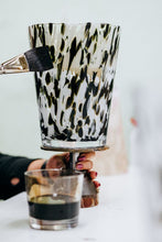 Candle with a patterned holder with a glass of dark liquid nearby.
