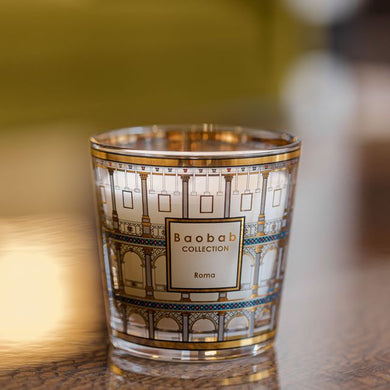 Decorative candle in a glass holder with 'Baobab Collection' branding on a reflective surface.