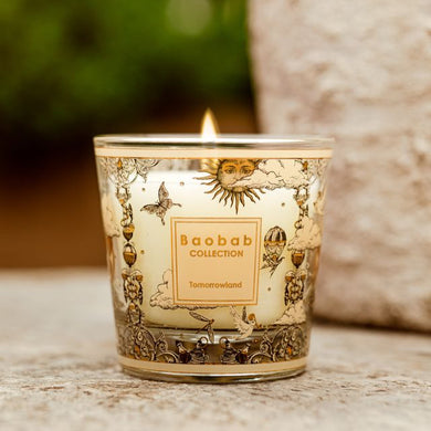Decorative candle with intricate designs and a visible brand label on a blurred natural background.
