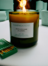 Candle labeled 'Highland Park Jalapeno' by Flamingo Estate with matches on a white surface.