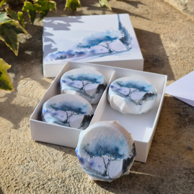 Soaps wrapped in cloth with artistic design in a white box on a textured surface.