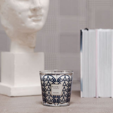 Candle with geometric design on a surface next to a marble bust and books.
