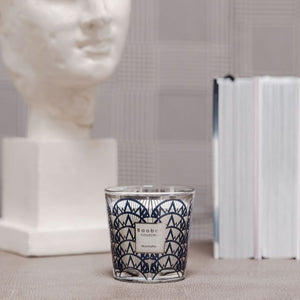 Candle with geometric design on a surface next to a marble bust and books.