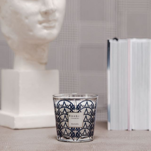 Candle with geometric design on a surface next to a marble bust and books.