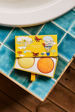 Two round soaps in a yellow box on a blue tiled surface.