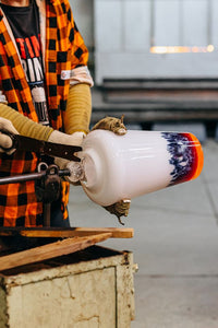 Person working with a glassblowing tool and a colorful glass piece in a workshop setting.