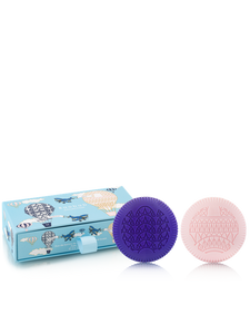 Two soaps, one purple and one pink, in front of a blue box with airplane designs on a white background.