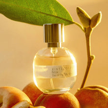 Perfume bottle labeled 'Kintsugi' Muza on peaches with a leaf on a warm-toned background
