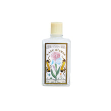 A clear glass bottle of L. T. Piver Lait D'Iris body milk with a cream-colored cap and a detailed botanical label featuring a pink iris flower, green leaves, and gold scrollwork.