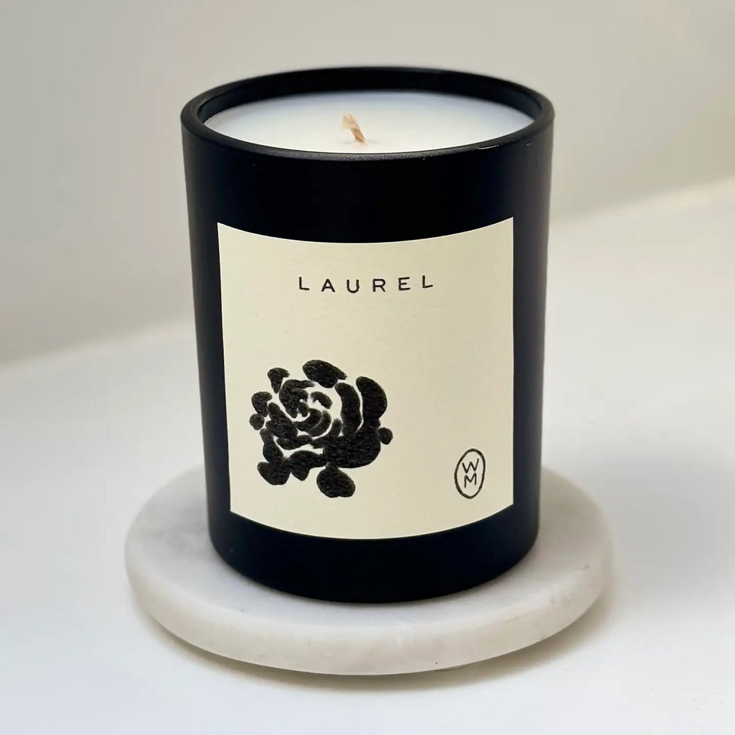 Candle in a black container with a white label featuring a black rose design on a light gray background.