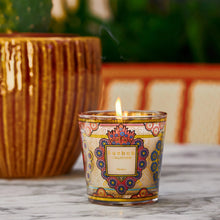 Decorative candle with intricate design on a marble surface, next to a potted plant.