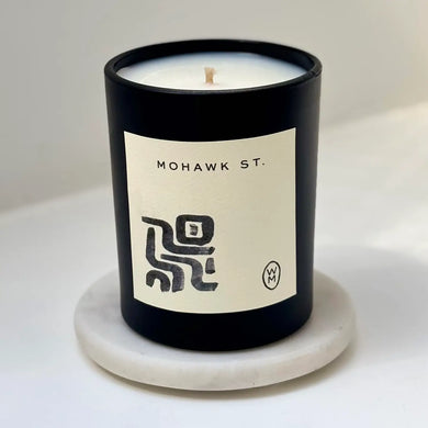 Candle in a black container with a label on a white surface