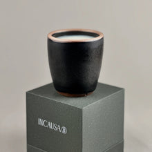 Black ceramic cup on a gray box with 'INCAUSA' branding against a light gray background
