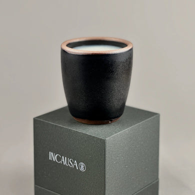 Black ceramic cup on a gray box with 'INCAUSA' branding against a light gray background