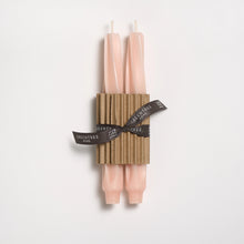 Two blush candles tied with a brown ribbon on a white background