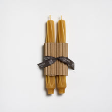 Two beeswax candles tied together with a brown paper wrap and black ribbon on a white background.