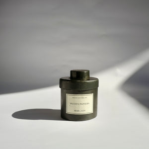 Black metal cylinder Mad et Len Candle Apothicaire Petite - Petits Papier in Black Wax. Matching lid cover on the candle. 