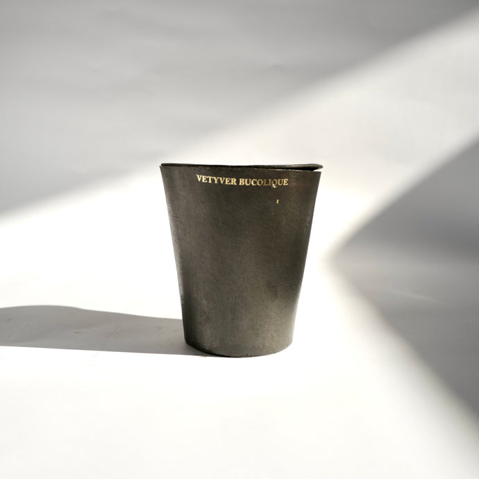 Black metal tapered Mad et Len Bougie Vestimentale Petite - VETYVER BUCOLIQUE (Black Wax) container with lid. Gold appliqué label of candle sent name. 