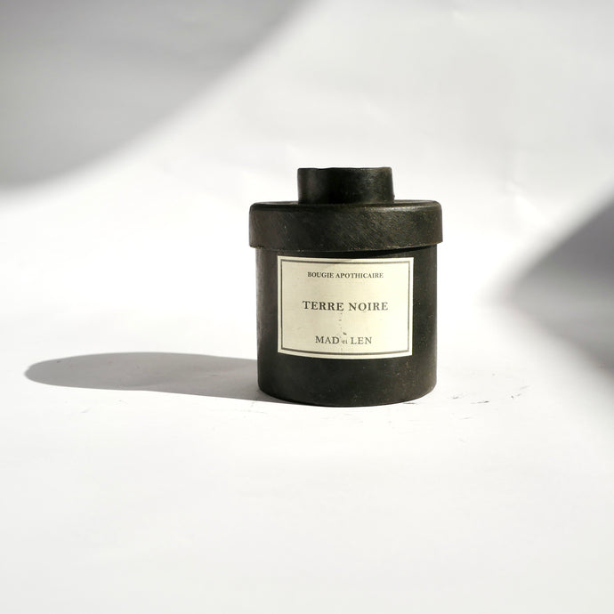 Black metal cylinder Mad et Len Candle Apothicaire Petite - TERRE NOIRE. Matching lid covering the candle. 