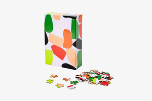 Box packaging with abstract graphic pattern of the Dusen Dusen Puzzle. Puzzle pieces scattered on a white surface.