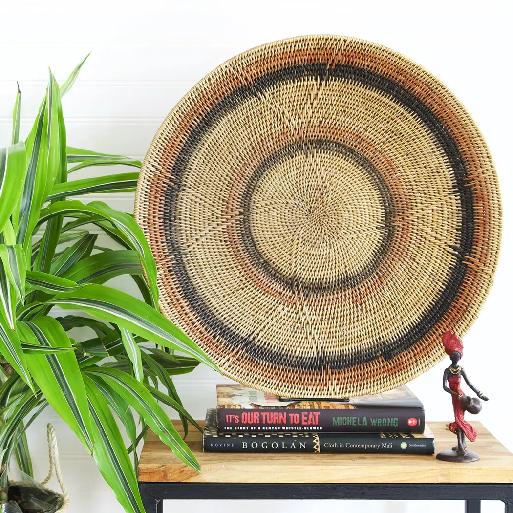 Makenge Root Wedding Baskets - Peach and Black Rings displayed on books with a tribal sculpture on a table. 