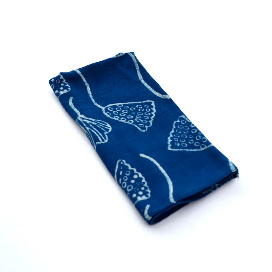 A folded Lana Napkin with blue and white indigo block print of water lily seed pods.  