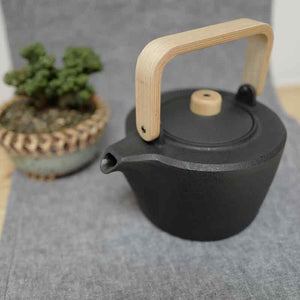 Chushin Kobo Cast Iron Pot with Oak Handle on a table runner. A succulent in the background. 