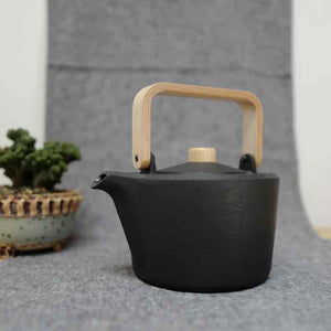Chushin Kobo Cast Iron Pot with Oak Handle on a table runner. A succulent plant in ceramic pot in the background. 
